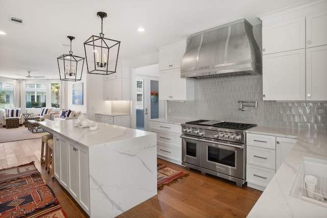 kitchen featuring wall chimney exhaust hood, dark wood-type flooring, white cabinetry, range with two ovens, and light stone countertops