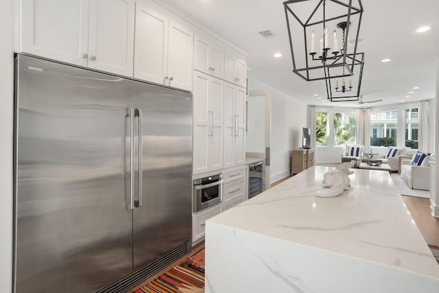 kitchen featuring white cabinetry, appliances with stainless steel finishes, light stone counters, and decorative light fixtures