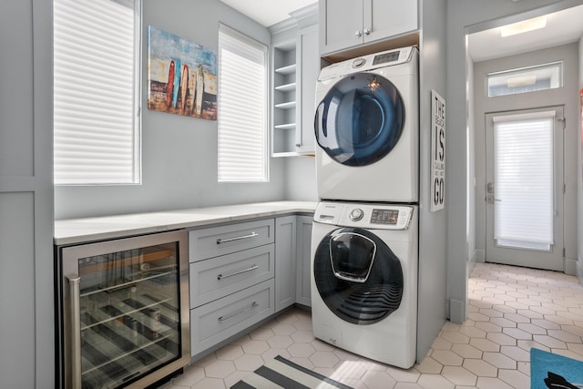 clothes washing area with cabinets, wine cooler, and stacked washing maching and dryer