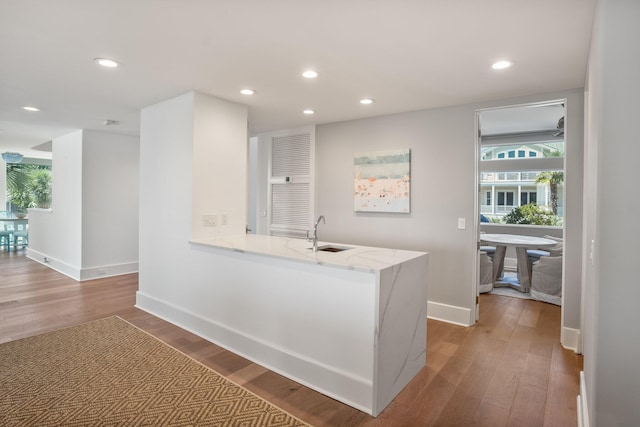 kitchen with kitchen peninsula, hardwood / wood-style floors, sink, and light stone counters