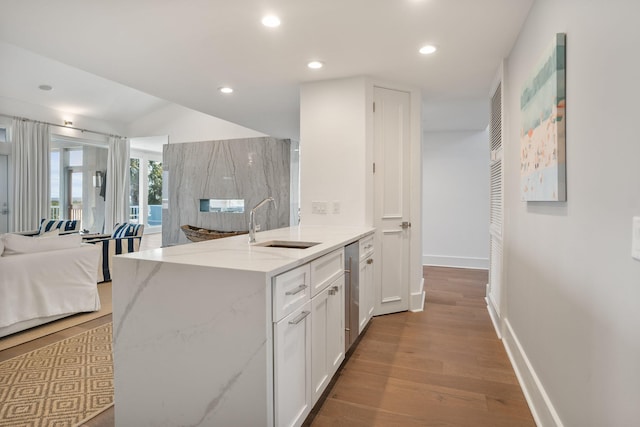 kitchen with light hardwood / wood-style floors, white cabinets, light stone countertops, stainless steel dishwasher, and sink