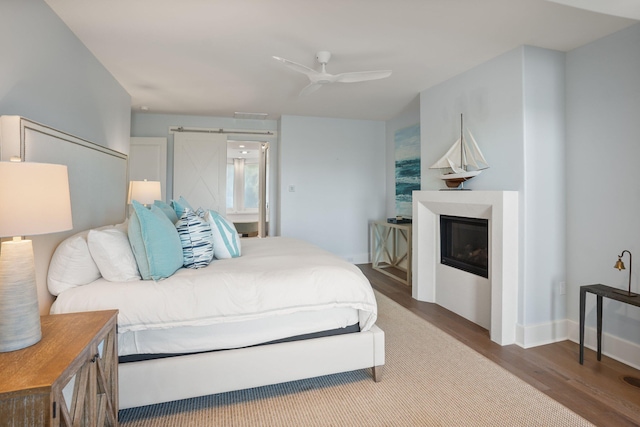 bedroom featuring a barn door, ceiling fan, and hardwood / wood-style flooring