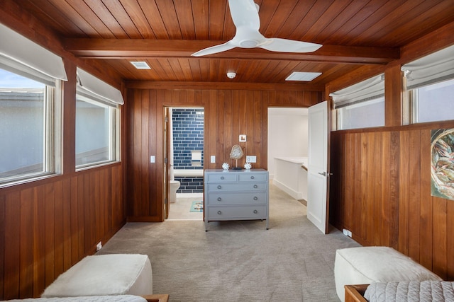 carpeted bedroom with connected bathroom, wooden ceiling, beam ceiling, ceiling fan, and wooden walls