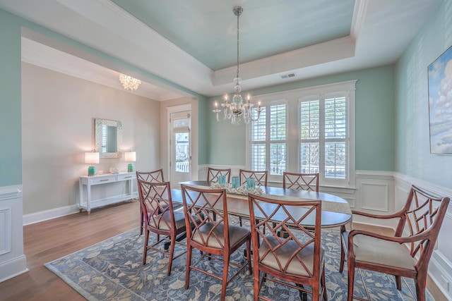 dining area featuring a tray ceiling, a wainscoted wall, visible vents, wood finished floors, and a chandelier