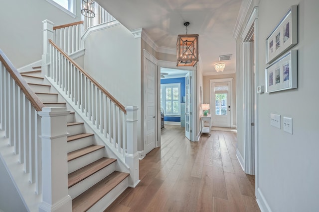 foyer entrance with baseboards, hardwood / wood-style flooring, visible vents, and crown molding