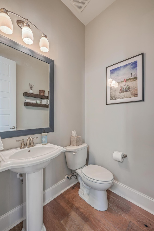 half bathroom featuring toilet, wood finished floors, visible vents, and baseboards