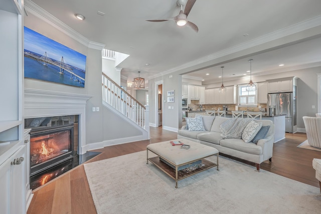 living area with a fireplace with flush hearth, stairway, wood finished floors, and crown molding