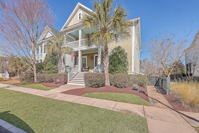 view of front of home featuring a balcony, covered porch, fence, and a front lawn