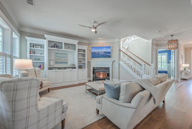 living room featuring a glass covered fireplace, crown molding, stairway, and wood finished floors