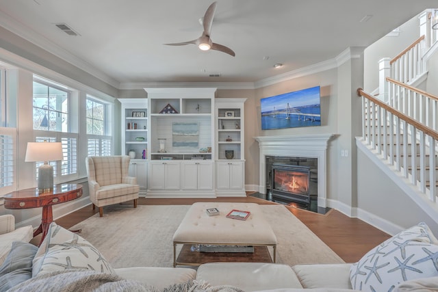 living room with visible vents, ornamental molding, a fireplace with flush hearth, wood finished floors, and stairs