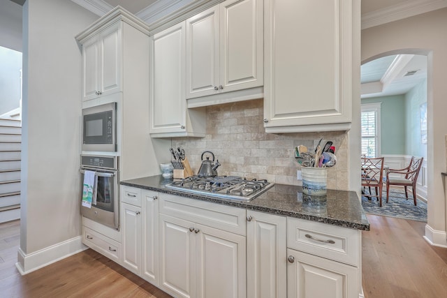 kitchen with arched walkways, white cabinets, light wood-style flooring, stainless steel appliances, and crown molding