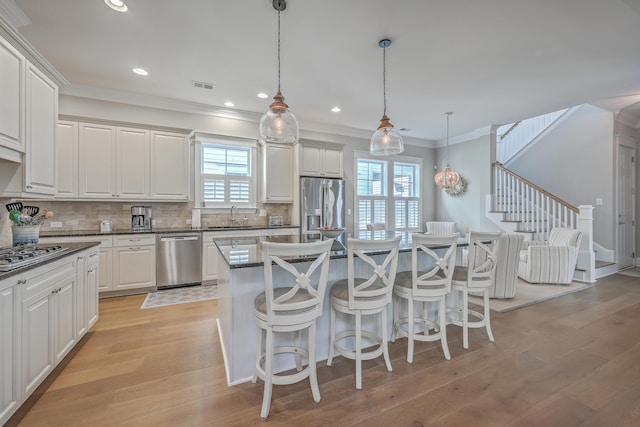 kitchen featuring decorative light fixtures, stainless steel appliances, dark countertops, white cabinets, and a sink