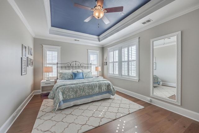 bedroom with dark wood-style floors, ornamental molding, a raised ceiling, and baseboards