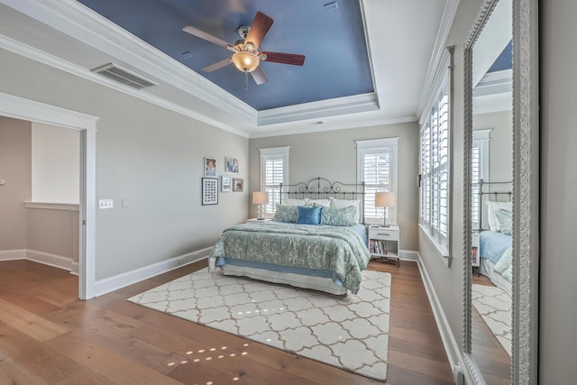 bedroom with a raised ceiling, visible vents, ornamental molding, wood finished floors, and baseboards