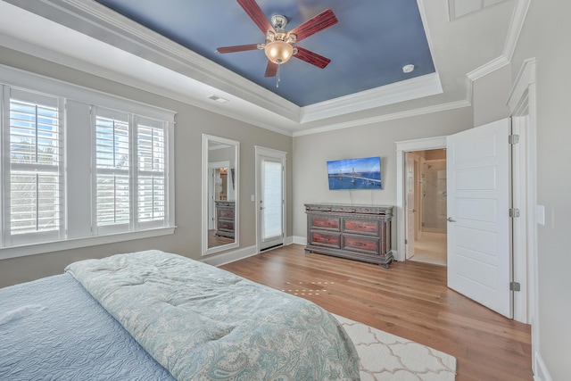 bedroom featuring baseboards, visible vents, a raised ceiling, wood finished floors, and crown molding