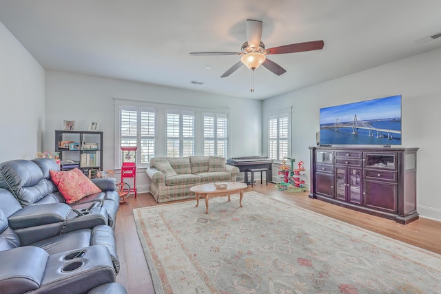 living area featuring light wood-type flooring, visible vents, ceiling fan, and baseboards