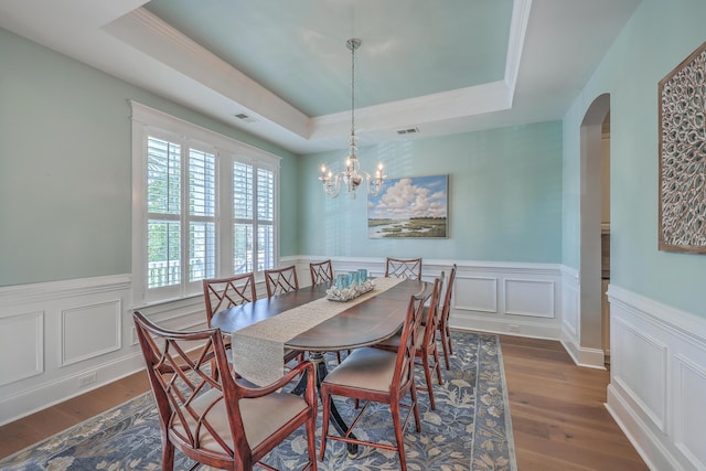 dining room featuring arched walkways, a wainscoted wall, wood finished floors, visible vents, and a raised ceiling