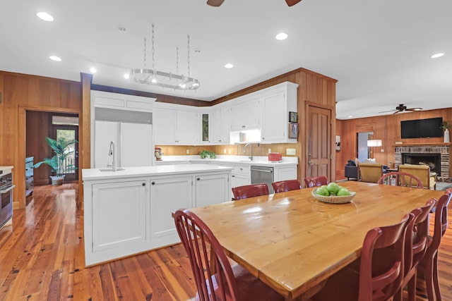 dining room featuring ceiling fan, wood walls, a brick fireplace, and wood finished floors