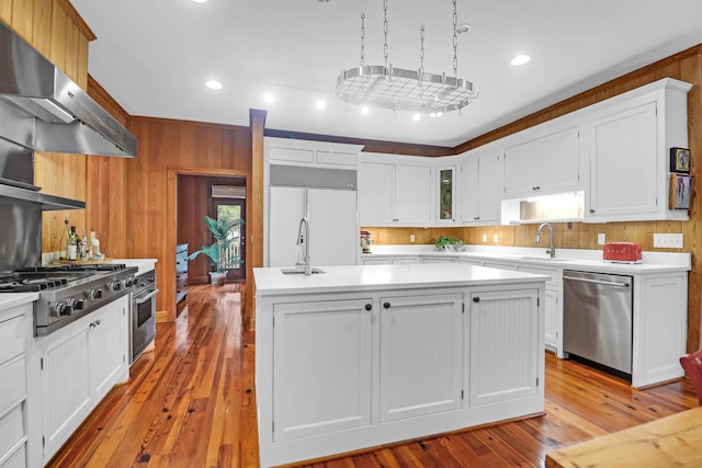 kitchen with stainless steel appliances, light countertops, a sink, wooden walls, and extractor fan