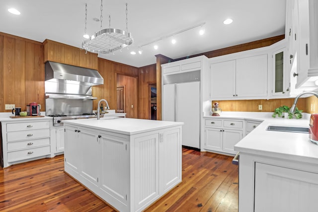 kitchen featuring dark wood-style floors, light countertops, paneled built in fridge, a sink, and extractor fan