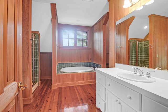 full bath featuring hardwood / wood-style flooring, vanity, wood walls, a shower stall, and a bath