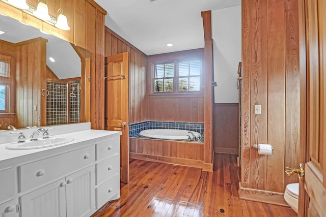 full bathroom featuring a garden tub, toilet, hardwood / wood-style flooring, wooden walls, and tiled shower