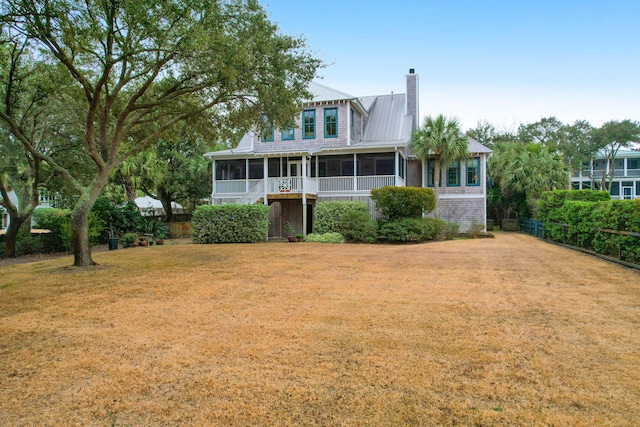 view of front facade with metal roof, fence, a sunroom, a front lawn, and a chimney