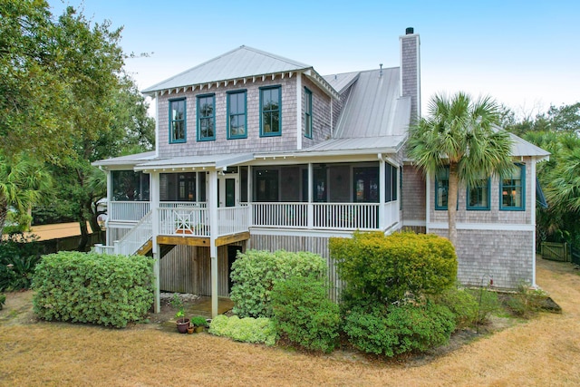 view of front of property with a sunroom, a chimney, a front lawn, and metal roof