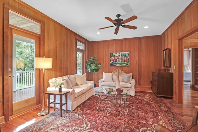 living area with a ceiling fan, wooden walls, and wood finished floors