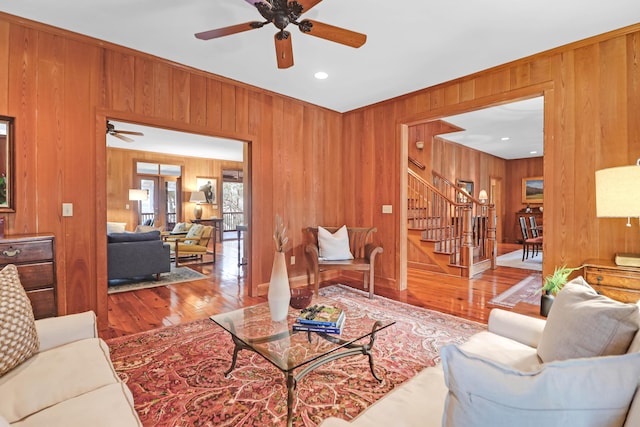 living room featuring stairs, ceiling fan, wood finished floors, and wooden walls