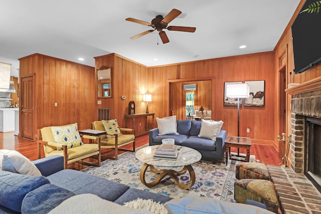 living area featuring ceiling fan, wooden walls, a fireplace, wood finished floors, and visible vents