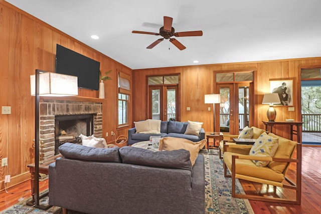 living room featuring french doors, wood walls, wood-type flooring, and a brick fireplace