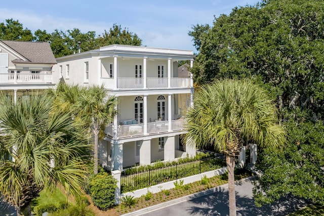 exterior space with a balcony, covered porch, stucco siding, french doors, and a fenced front yard