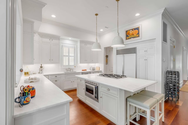 kitchen featuring a kitchen breakfast bar, crown molding, a sink, built in appliances, and wood finished floors