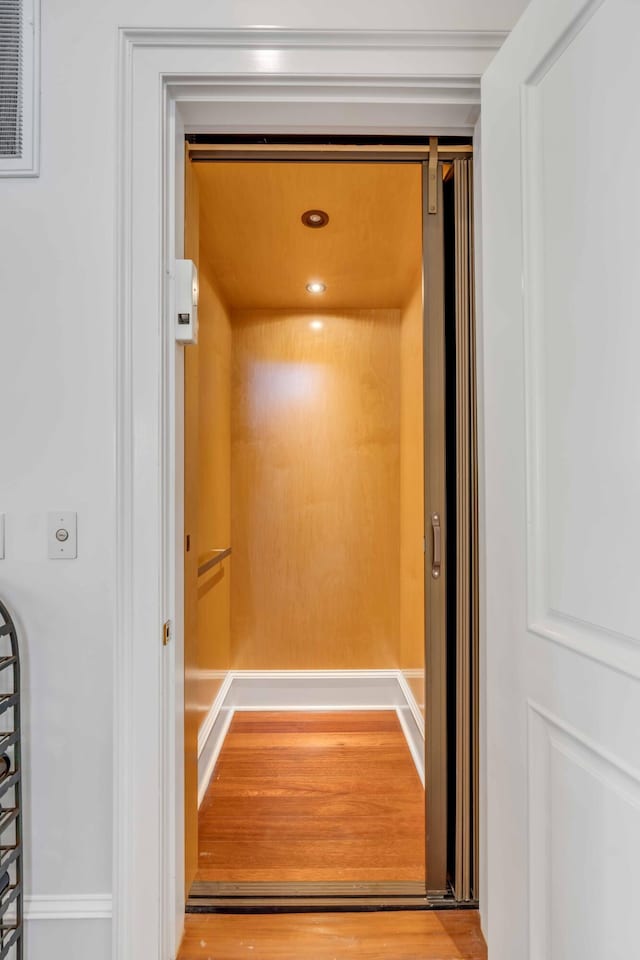 interior details featuring elevator, wood finished floors, and visible vents
