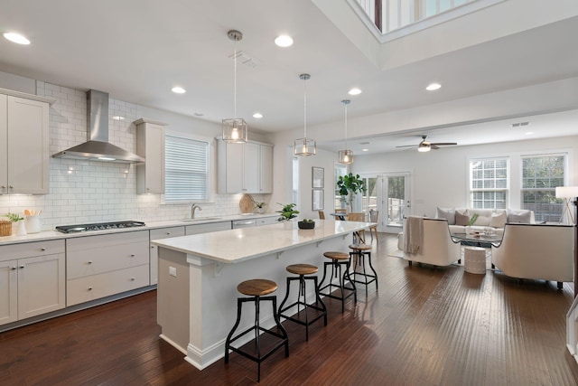 kitchen with a kitchen breakfast bar, hanging light fixtures, a center island, white cabinetry, and wall chimney range hood