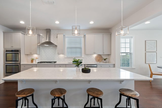 kitchen featuring a large island, wall chimney exhaust hood, and pendant lighting