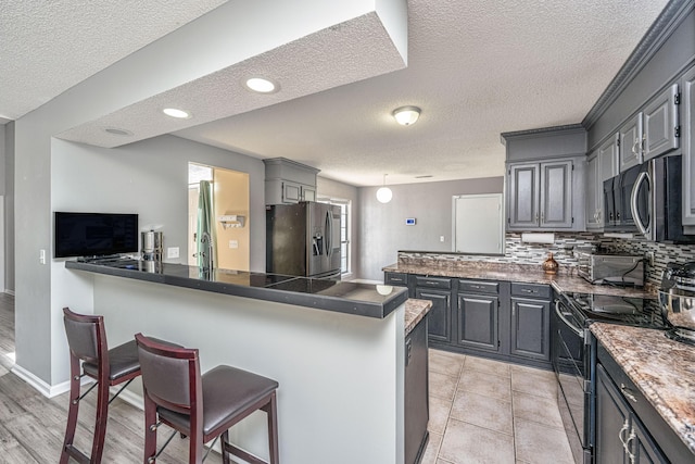 kitchen featuring stainless steel appliances, a breakfast bar, a peninsula, gray cabinets, and backsplash