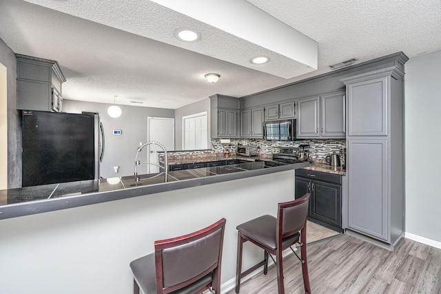 kitchen with a breakfast bar area, stainless steel appliances, dark countertops, gray cabinets, and a sink