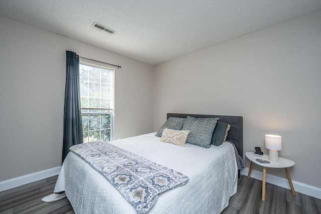 bedroom with a textured ceiling, dark wood-type flooring, visible vents, and baseboards