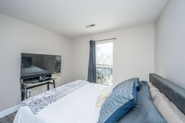 bedroom with a textured ceiling, wood finished floors, and visible vents