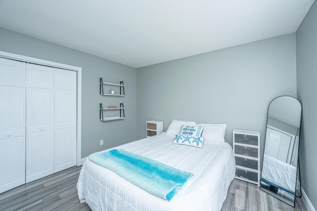 bedroom with a closet, a textured ceiling, baseboards, and wood finished floors