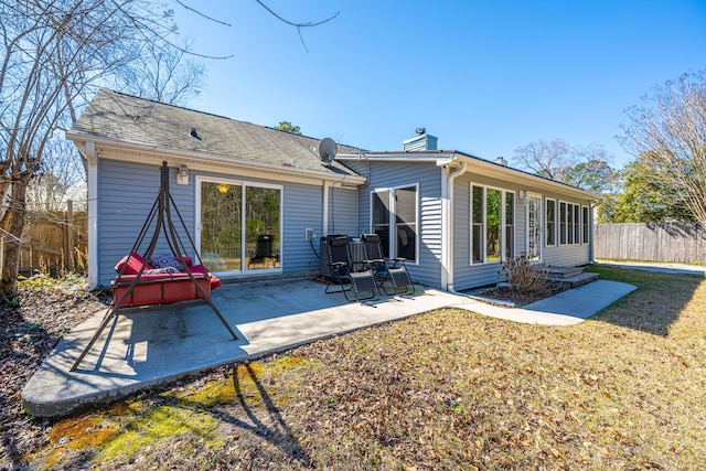 back of property with fence, a yard, roof with shingles, a chimney, and a patio area