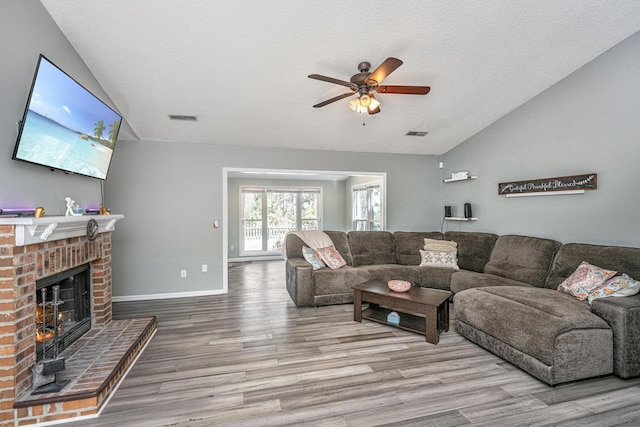 living area with visible vents, a brick fireplace, vaulted ceiling, wood finished floors, and baseboards