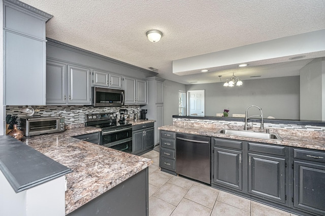 kitchen with gray cabinets, backsplash, appliances with stainless steel finishes, a sink, and a peninsula