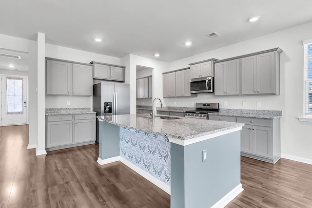 kitchen featuring an island with sink, light stone countertops, dark hardwood / wood-style floors, gray cabinetry, and stainless steel appliances