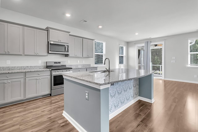 kitchen featuring light hardwood / wood-style floors, appliances with stainless steel finishes, sink, and an island with sink