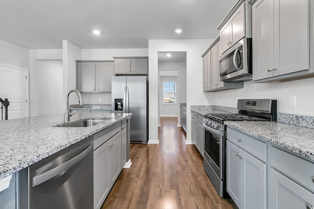 kitchen with dark wood-type flooring, sink, gray cabinets, appliances with stainless steel finishes, and light stone counters