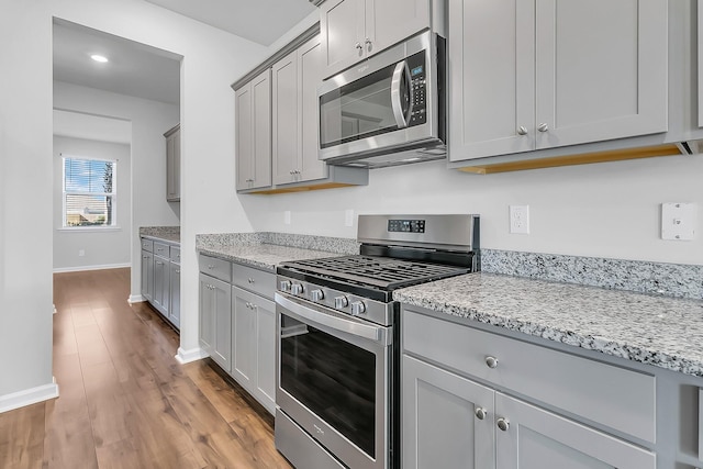 kitchen featuring light stone countertops, appliances with stainless steel finishes, light hardwood / wood-style flooring, and gray cabinets