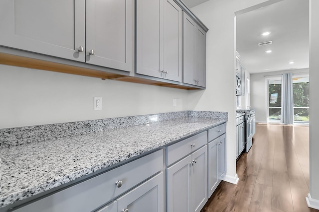 kitchen with gray cabinetry, light stone counters, appliances with stainless steel finishes, and dark hardwood / wood-style floors